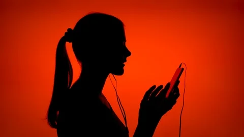 Silhouette of young woman put on ear-phones and listen to music on smart phone Stock Footage