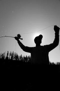 Silhouetted angler casting a fly rod in summer, black and white. Foto stock