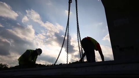 Silhouetted Construction Workers Attach Crane Chains to Load 库存影片 69246982