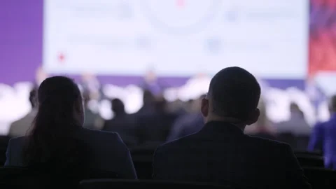 Silhouetted couple watching illuminated screen backlit attendees dark auditorium Stock Footage 328905166