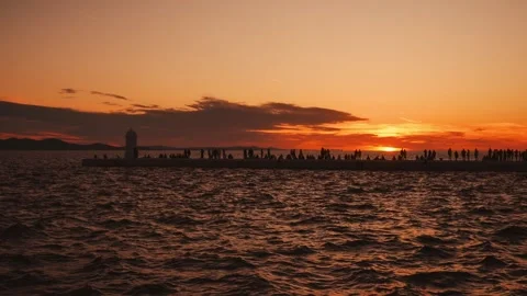 Silhouetted crowd on old town Zadar pier with lighthouse watching sunset over Vídeo Stock 344453824