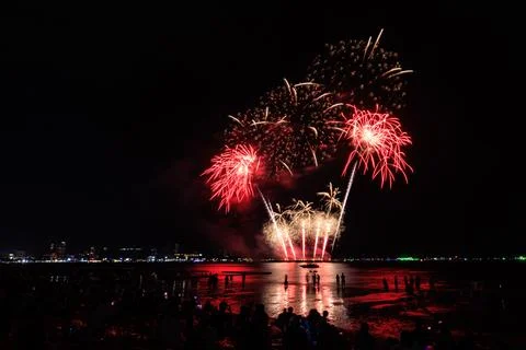 Silhouetted Crowd Watching Fireworks Display Exploding Over Ocean Beach At .. Stock Photos