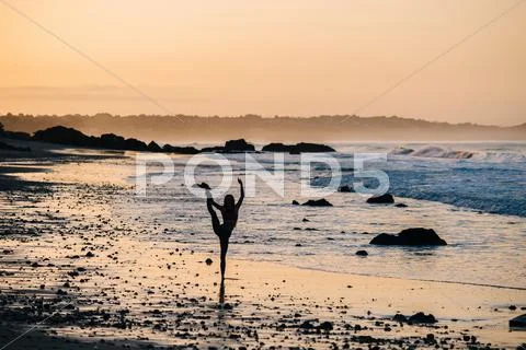 Silhouetted Female Ballet Dancer Poised On One Leg At Sunset On Beach, Los
