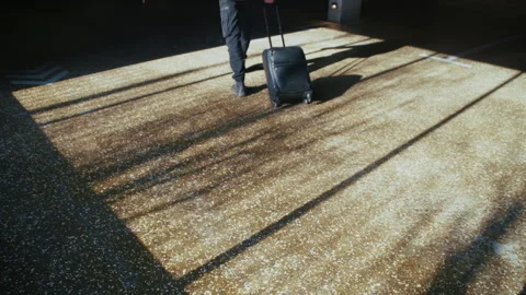 Silhouetted Figure with Rolling Suitcase in Sun-Filled Concrete Garage Video stock 335474030