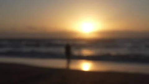 Silhouetted figure standing on blurred image of a sunset in a sandy beach 库存影片 309295525