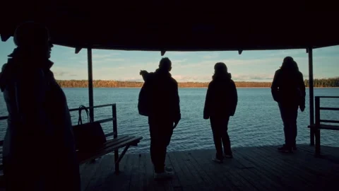 Silhouetted figures standing on lakeside dock at sunset Stock Footage 301125218