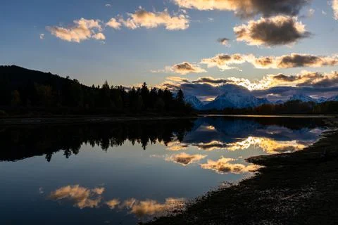 Silhouetted forest with cloudy sky reflecting on Snake river. Stock Photos