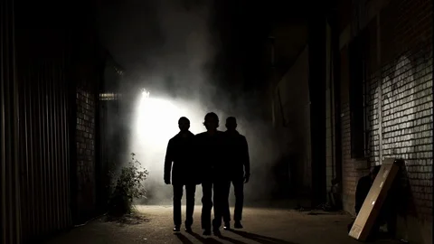 Silhouetted group of three men walk down a steamy alley at night Stock Footage