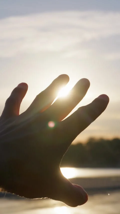 Silhouetted Hand Reaching Toward Bright Sunset Sun Flare Over Water Stock Footage 345425107