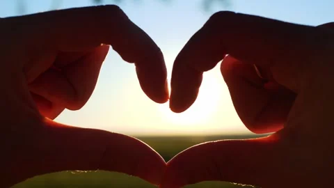 Silhouetted hands forming a heart shape against a bright sunrise... Stockbeeldmateriaal 322811895