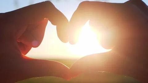 Silhouetted hands forming a heart shape against a bright sunrise... Stock Footage 322811904
