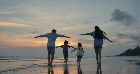 Silhouetted happy asian family playing and having fun on the beach at sunset. Stock Footage
