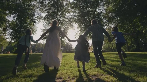 Silhouetted happy caucasian family running towards sun having fun in city park Stock Footage