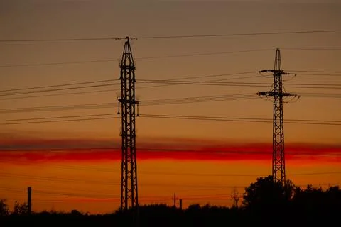 Silhouetted high voltage lines span tranquil countryside at dusk Stock Photos