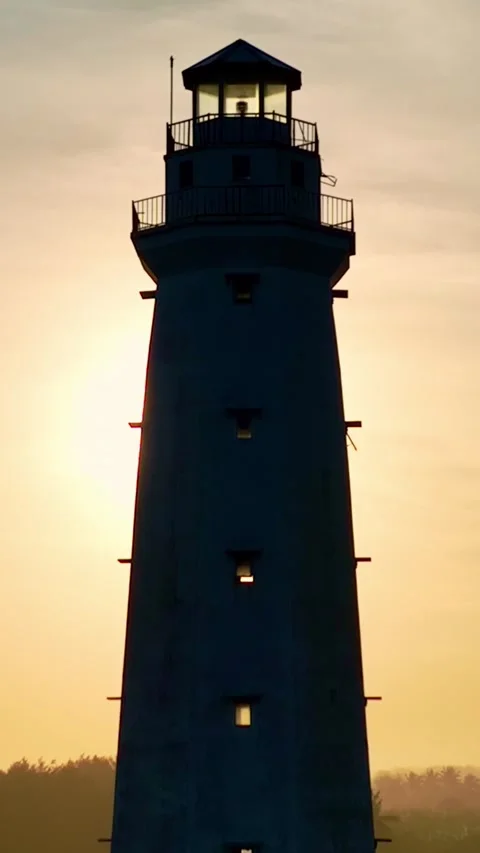 Silhouetted lighthouse glowing against warm sunset sky Vídeo Stock 335432376
