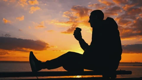 Silhouetted Man at Sunset Drinks Coffee on a Bench Stock Footage 255518053