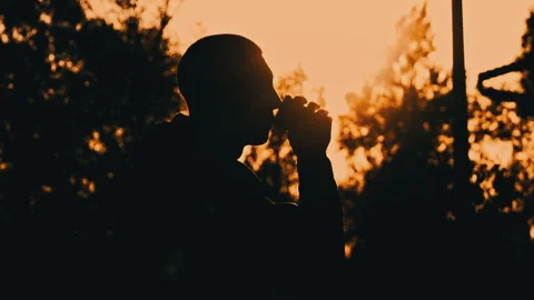 Silhouetted Man at Sunset Drinks Coffee on a Bench Stock Footage 255523162