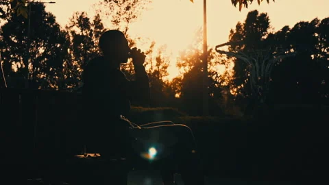 Silhouetted Man at Sunset Drinks Coffee on a Bench Stock Footage 255586985
