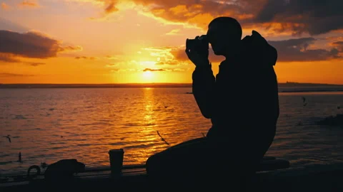 Silhouetted Man at Sunset Drinks Coffee on a Bench Stock Footage 256088380