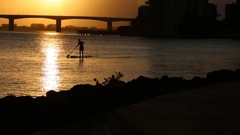 Silhouetted man on surfboard. Beautiful dramatic sunset on the gulf. 스톡 동영상 115910029