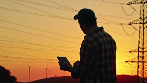 Silhouetted Man Using Tablet Near Power Lines at Sunset 库存影片 344564527