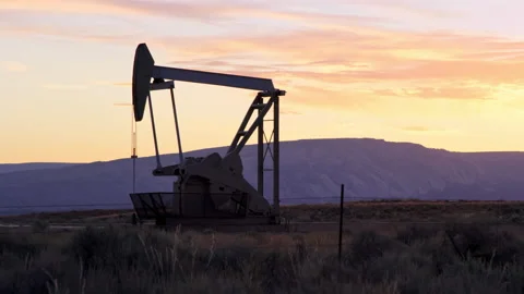 Silhouetted oil pump rig operates at sunrise in Vernal Utah oil field Video stock 202202170
