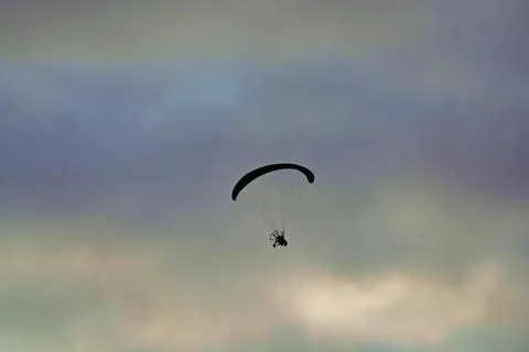 Silhouetted paramotor glides high across softly clouded sky 写真素材