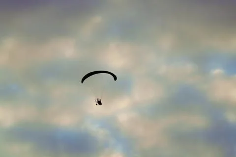 Silhouetted paramotor glides high across softly clouded sky 库存照片