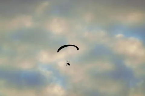 Silhouetted paramotor glides high across softly clouded sky Stock Photos