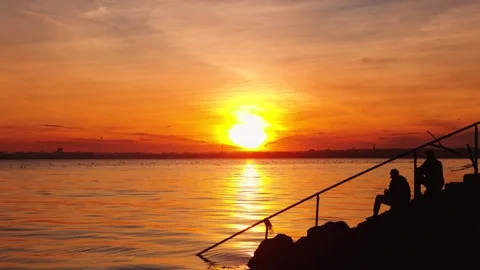 Silhouetted People Sitting on Seaside Steps at Sunset with Birds Flying, Bull Stock Footage 334700916