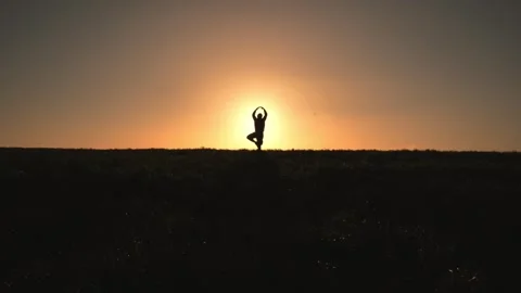 Silhouetted person doing yoga in front of sun at sunset on top of hill Video stock 278721965