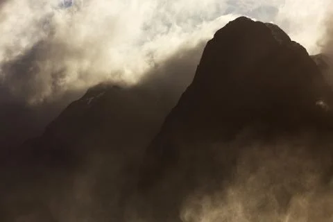 Silhouetted powerful, mist and cloud shrouded mountain peaks Stock Photos