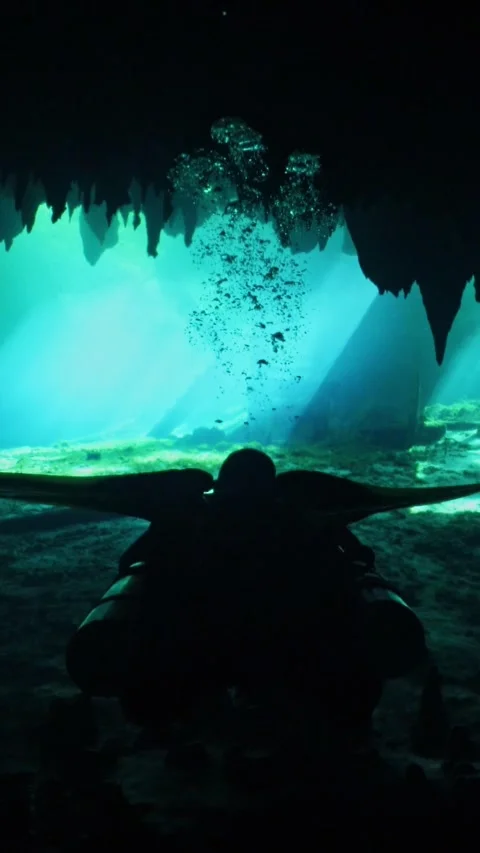 Silhouetted scuba divers exploring a sunlit underwater cave with stalactites and Vídeos de archivo 331341370