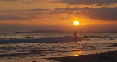 Silhouetted surfer surfing waves during sunset at California beach Stock Footage