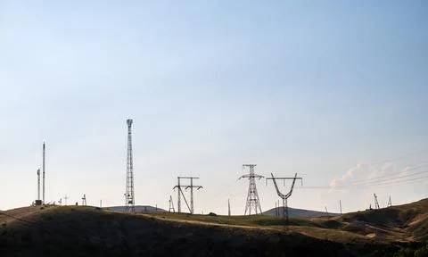 Silhouettes of electrical infrastructure atop rolling hills under open sky Stock Photos