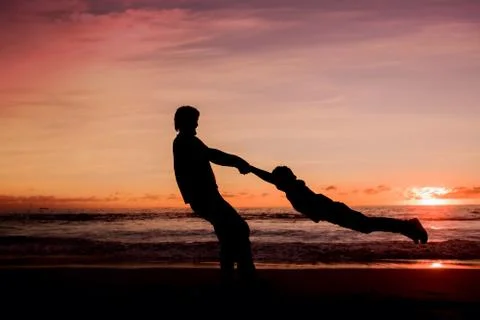 Silhouettes of father spinning his son around on sunset Stock Photos