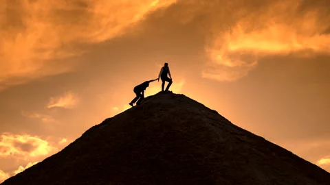 Silhouettes help each other on top of the mountain Stock Footage 130993034