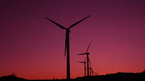 Silhouettes of modern wind turbines with rotating blades against a red sunset Stock Footage 346246983