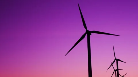 Silhouettes of modern wind turbines with rotating blades against a purple sunset Stock Footage 346776228