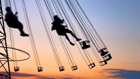 Silhouettes of people ride on the chained carousel against sunset sky - slow mo Stock Footage 340446327