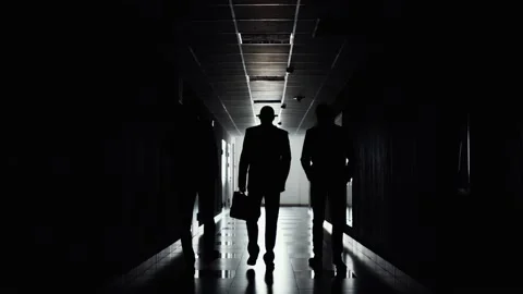 Silhouettes of three businessmen walking in direction of light along corridor. Stock Footage