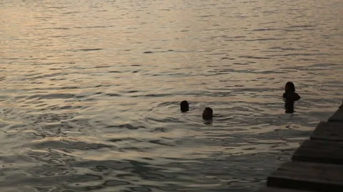 Silhouettes of three people bathing in the sea by dusk Stock Footage 277872471