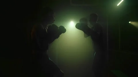 Silhouettes of two boxers. Men are boxing in a dark ring. Twilight diffused Stock Footage 228726336