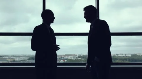 Silhouettes of two businessmen standing by the window and talking. Stock Footage 92735993