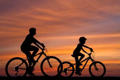 Silhouettes of two cyclists against the background of the sunset Stock Photos