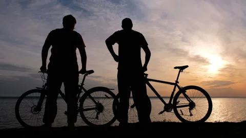 Silhouettes Of Two Cyclists on the coast of sea at sunset time. Video stock 89787729