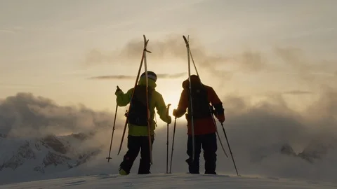 Silhouettes of two freeride skiers talking while watching sunrise in Swiss Alps Stock Footage 129086469