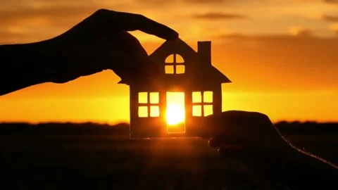 Silhouettes of two hands hold up a paper cutout of a house against a stunnin Stock Footage 316280976
