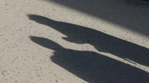 Silhouettes of Two People Cast as Shadows on Sunlit Pavement Stock Footage 336221154
