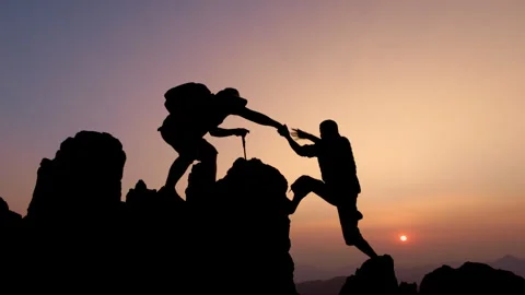 Silhouettes of two people climbing on mountain and helping. Teamwork of two.. Stock Footage 336955168